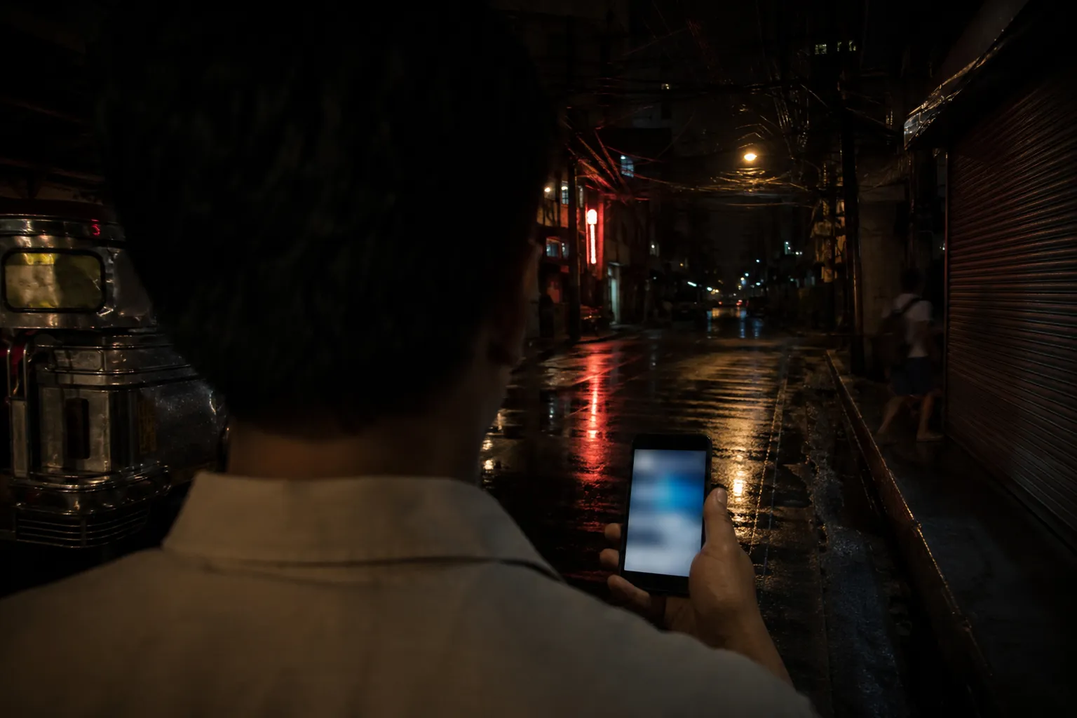 A hand holding a lit phone on a wet Manila side street at night