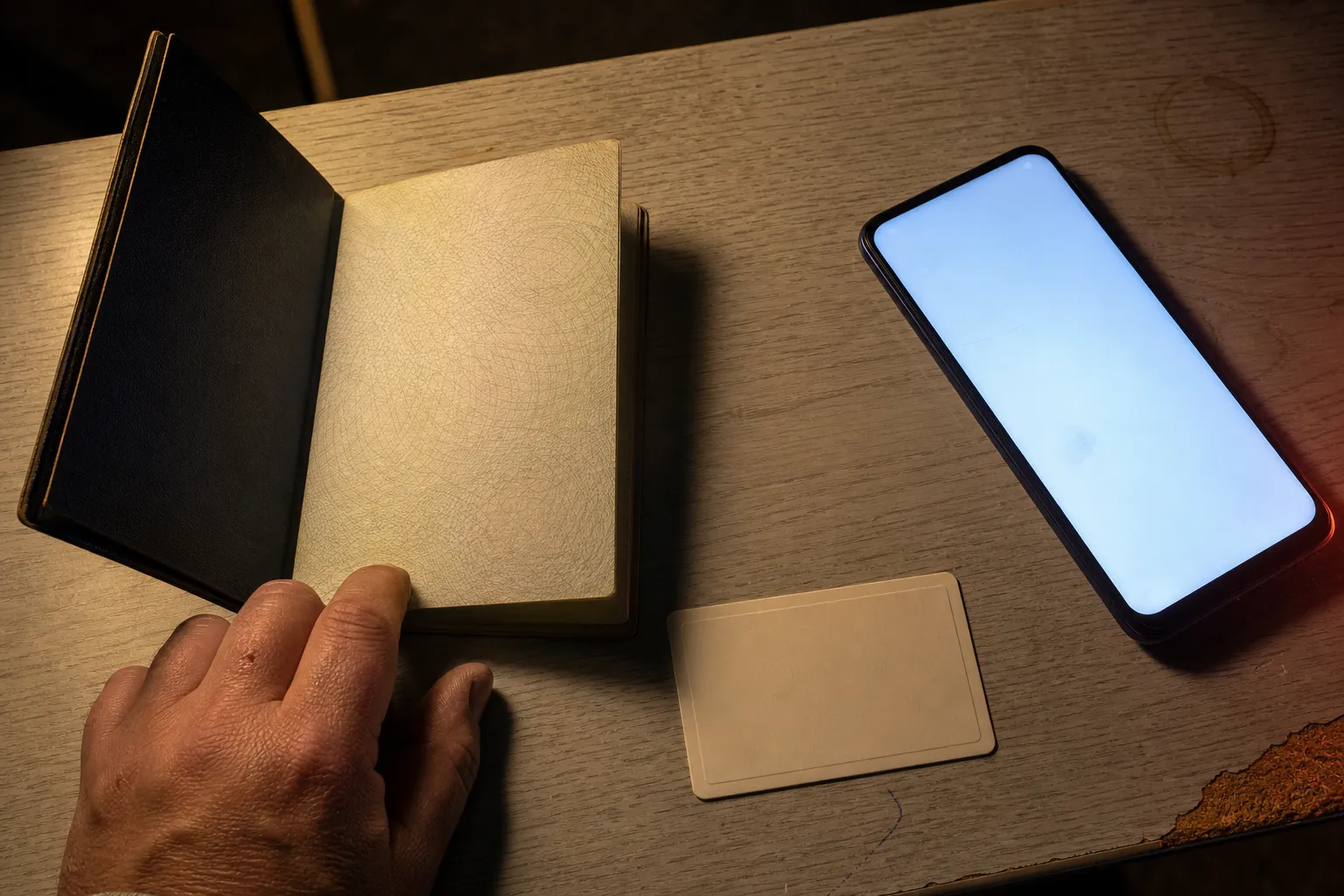 Passport and identity card beside a glowing phone on a cheap hotel desk at night